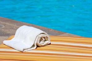 A rolled white towel on a striped lounge chair by a pool.