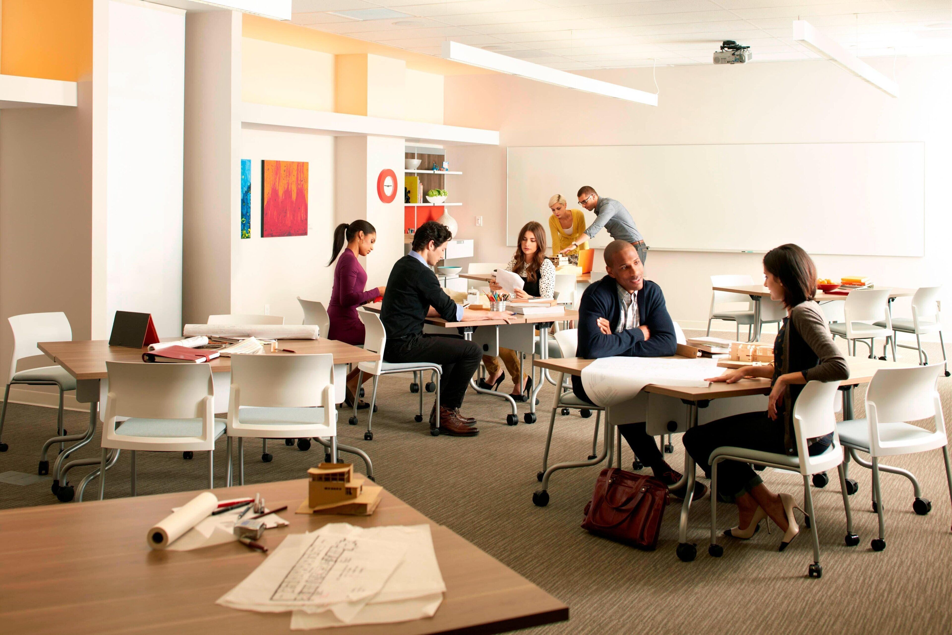A modern conference room with white chairs, tables, and a whiteboard.