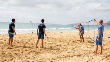 Partido de voleibol de playa con jugadores vestidos de azul y uno con una camisa oscura.