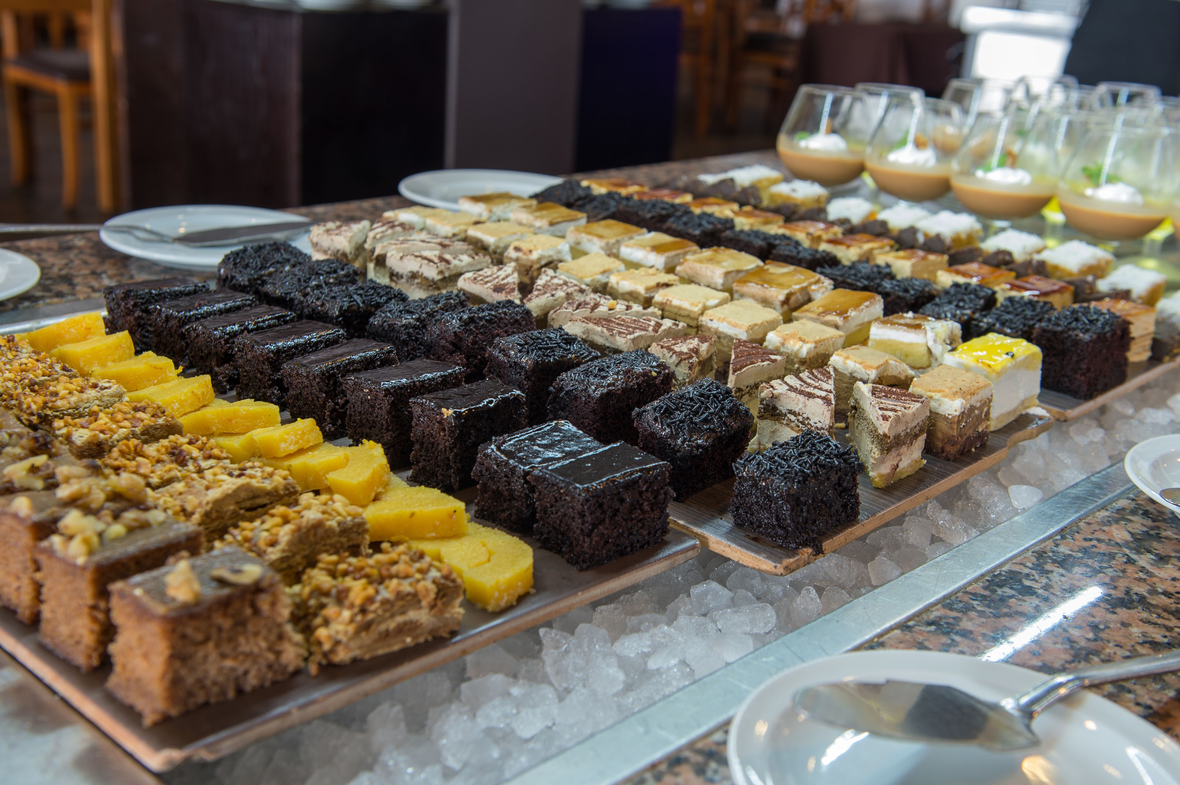 Une variété de desserts présentés sur un plateau, accompagnés de glaçons, de verres remplis de boissons et d’une cuillère posée sur une table.