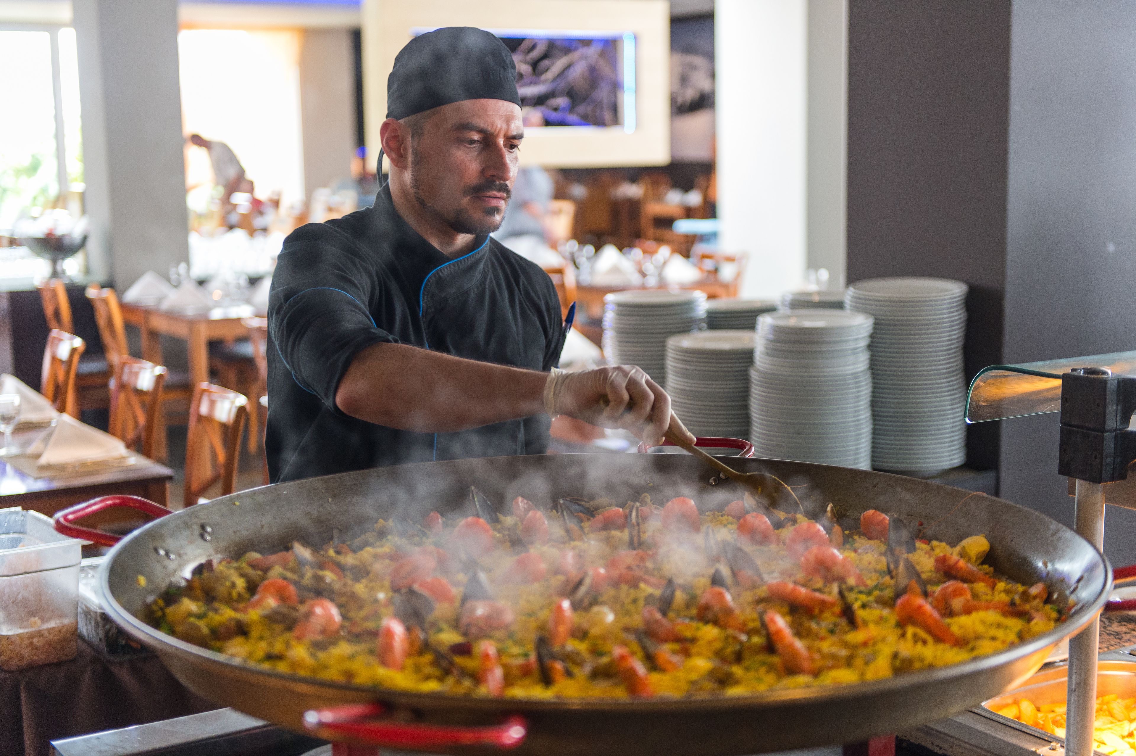 A chef cooking a large pan of paella with seafood and vegetables.