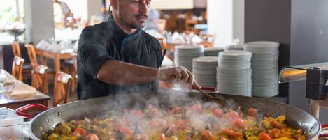A chef cooking a large pan of paella with seafood and vegetables.