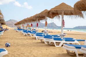 Una playa con filas de tumbonas y sombrillas de paja.