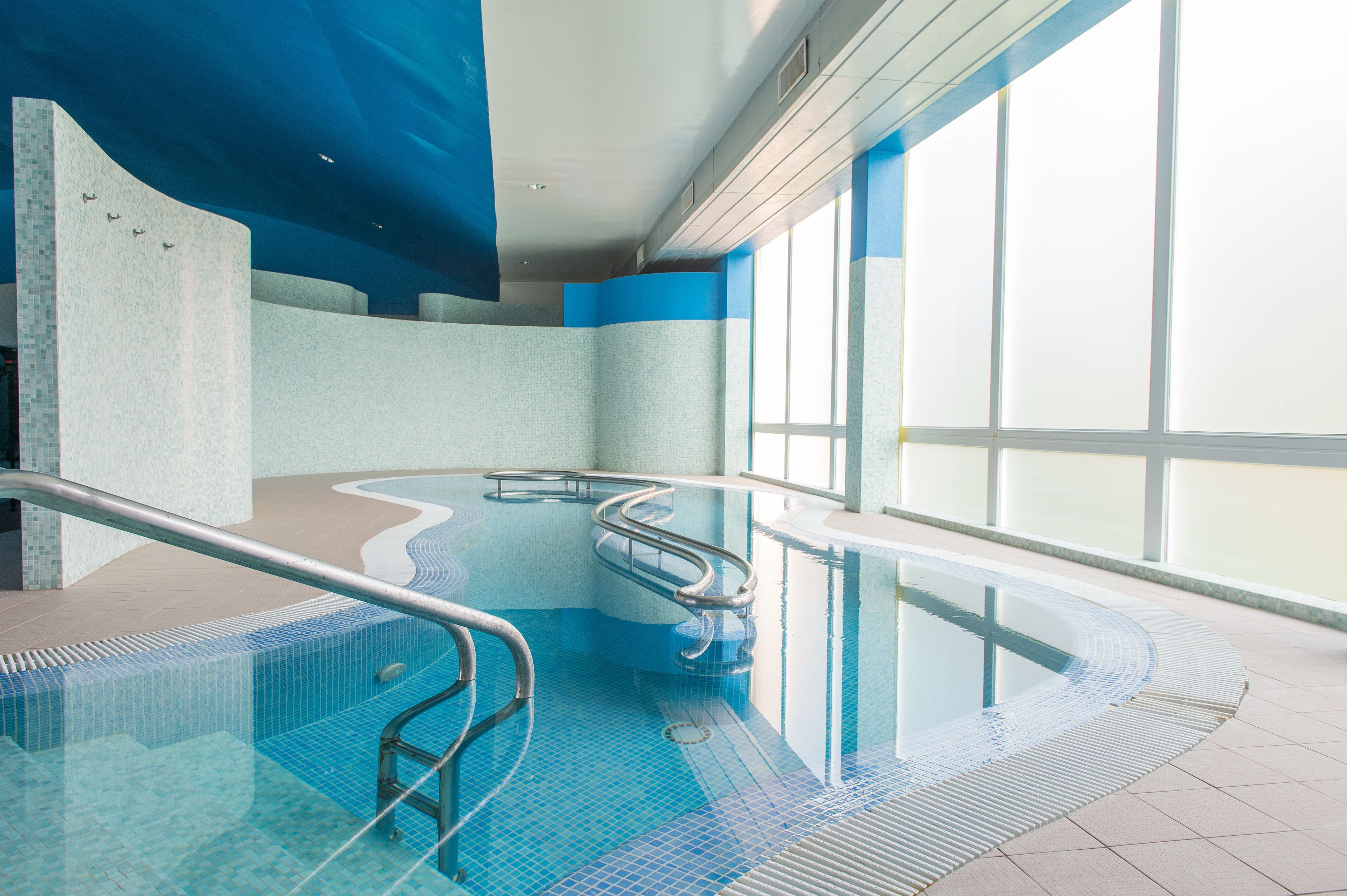 Una piscina interior con agua cristalina azul, diseño curvo y barandilla de metal.