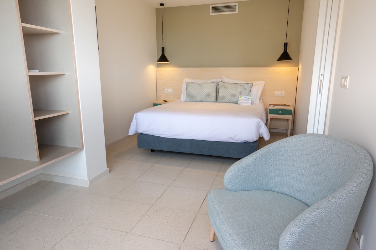 A bedroom with a bed, a chair, a nightstand, and a shelf unit.