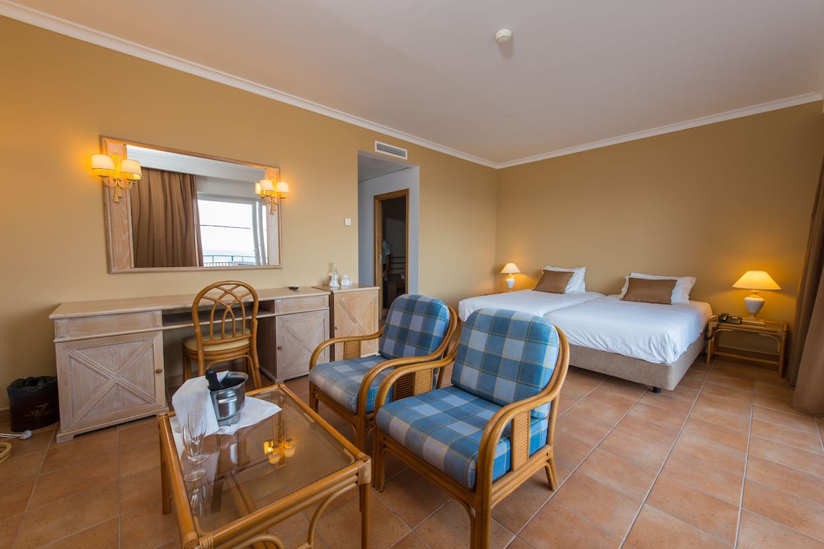 A hotel room with a bed, a desk with a chair, a small table with a glass, and a mirror.