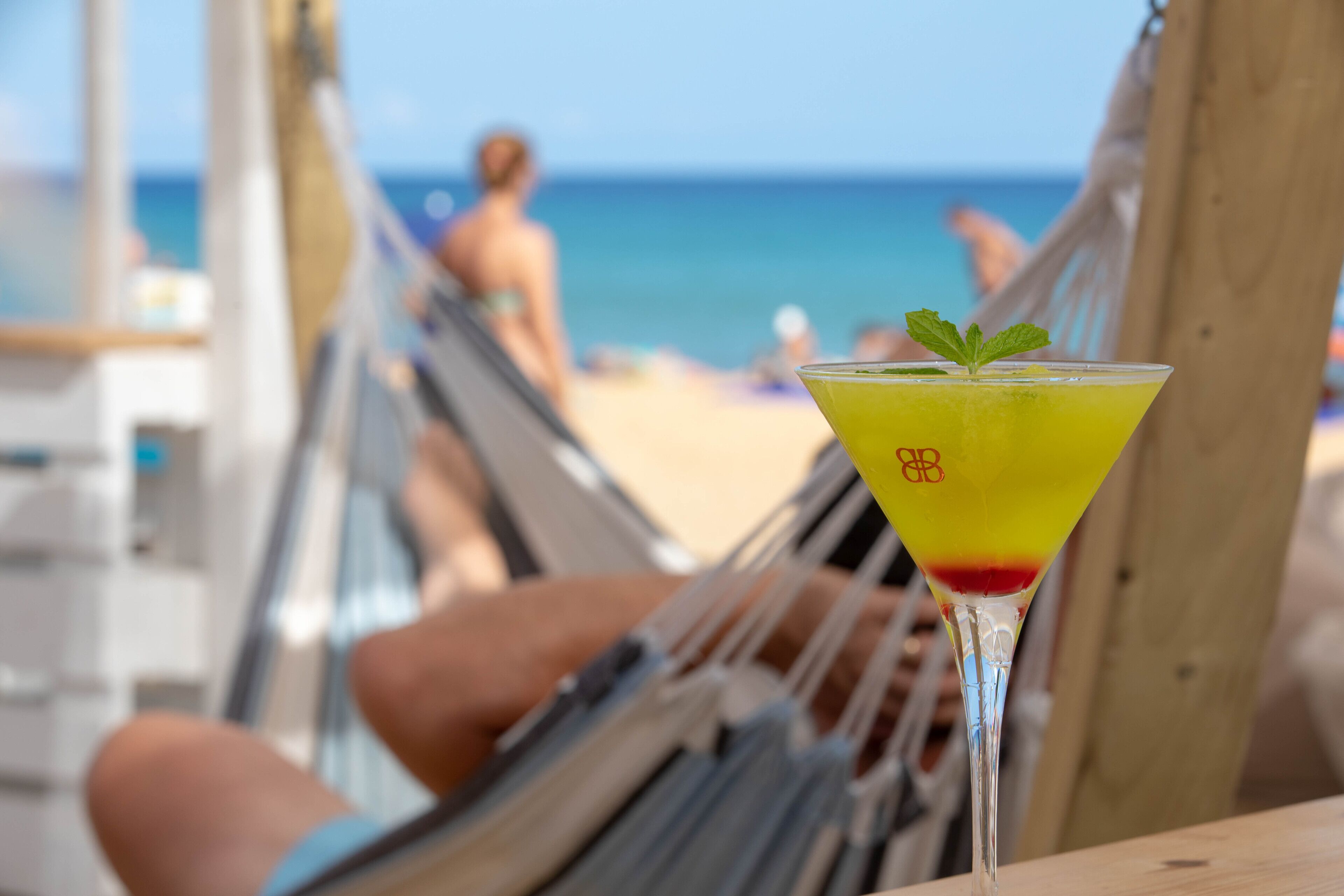 Une scène de plage avec un hamac et un verre à martini contenant une boisson jaune.
