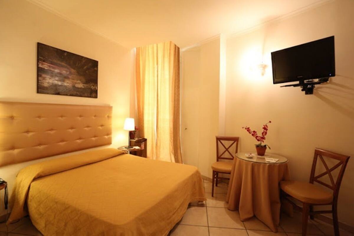 A hotel room with a large bed, a television mounted on the wall, a small table with a chair, and a painting on the wall.