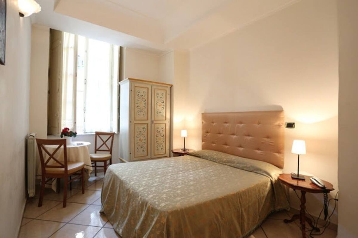 A bedroom with a large bed, two bedside tables with lamps, a wooden chair, a small table with flowers, and a cabinet.