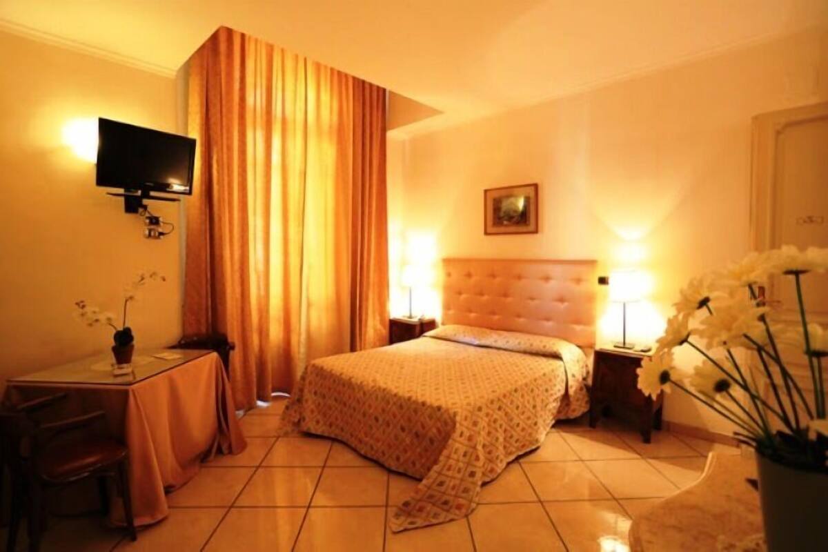 A hotel room with a bed, a desk with a chair, a television mounted on the wall, and a painting on the wall.