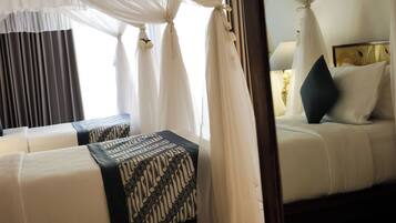 A hotel room with a canopy bed, two bedside tables with patterned cushions, and a view of the outside through sheer curtains.