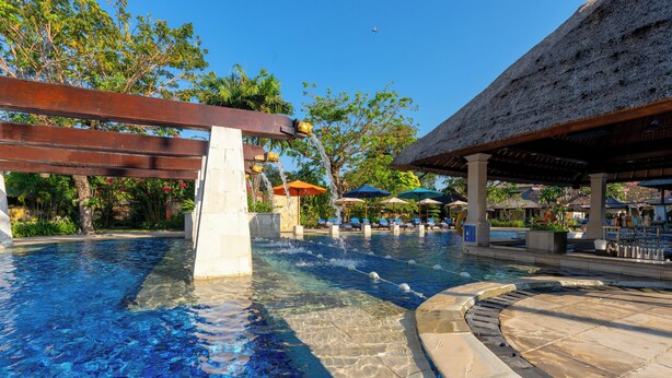 A swimming pool with clear blue water, surrounded by lounge chairs and umbrellas, and a thatched-roof structure. - Rama Beach Resort and Villas (Kuta)