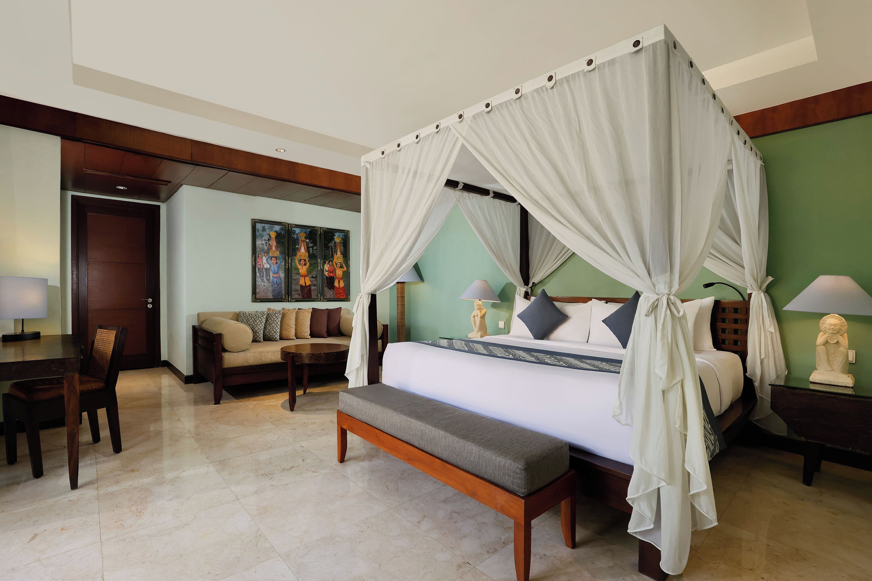 A bedroom with a four-poster canopy bed, a bench, a sofa, a dining table, and a statue on a nightstand.