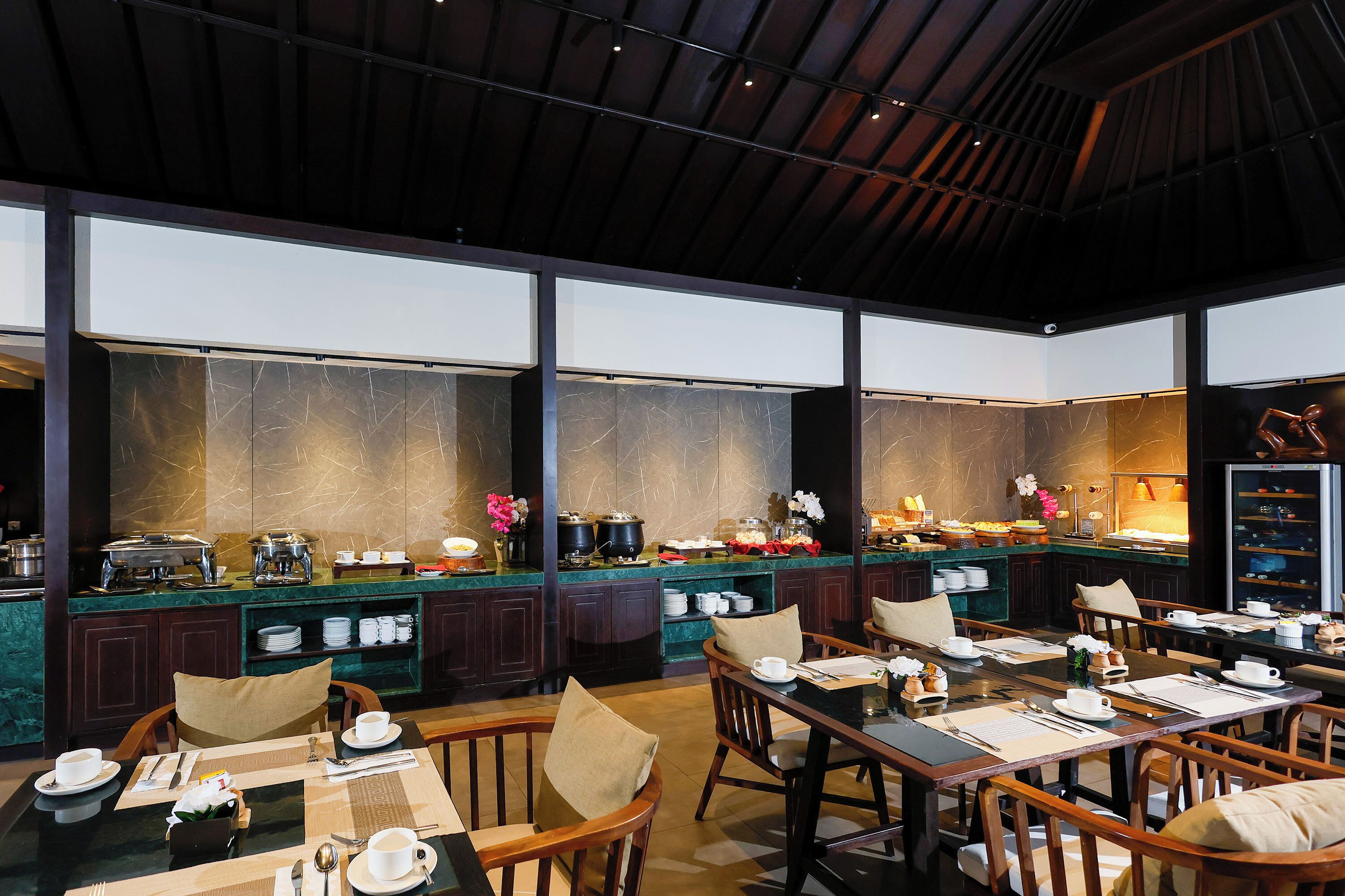 A spacious dining area with multiple tables and chairs, a buffet counter with various food items, and a large window providing a view of the interior.