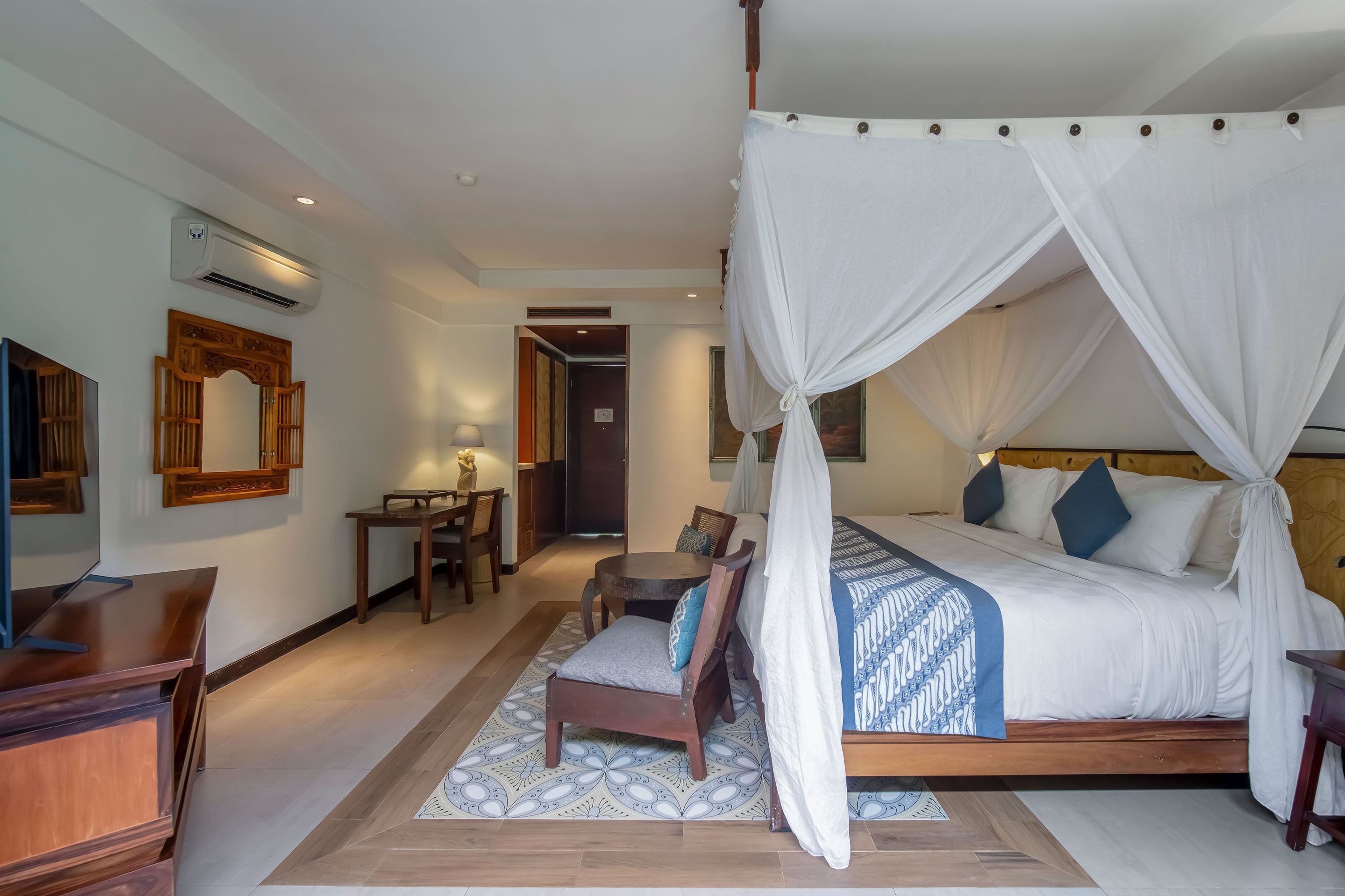 A bedroom with a four-poster bed, a desk, a chair, and a small table.