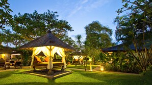 A thatched-roof gazebo with a bench and cushions, surrounded by lush greenery and a well-maintained lawn. - Rama Beach Resort and Villas (Kuta)