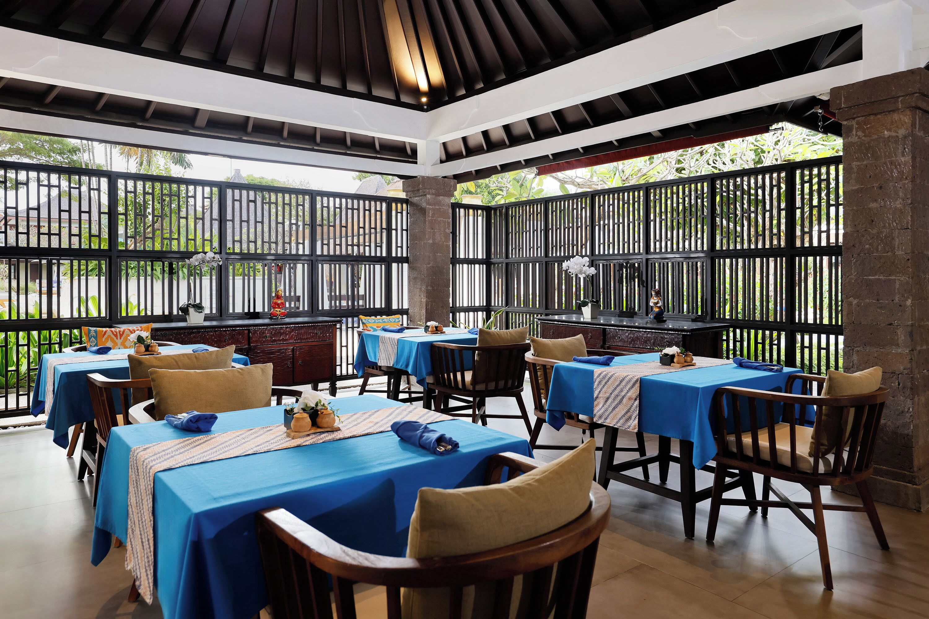 Un área de comedor al aire libre con mesas cubiertas de manteles azules y sillas de madera.