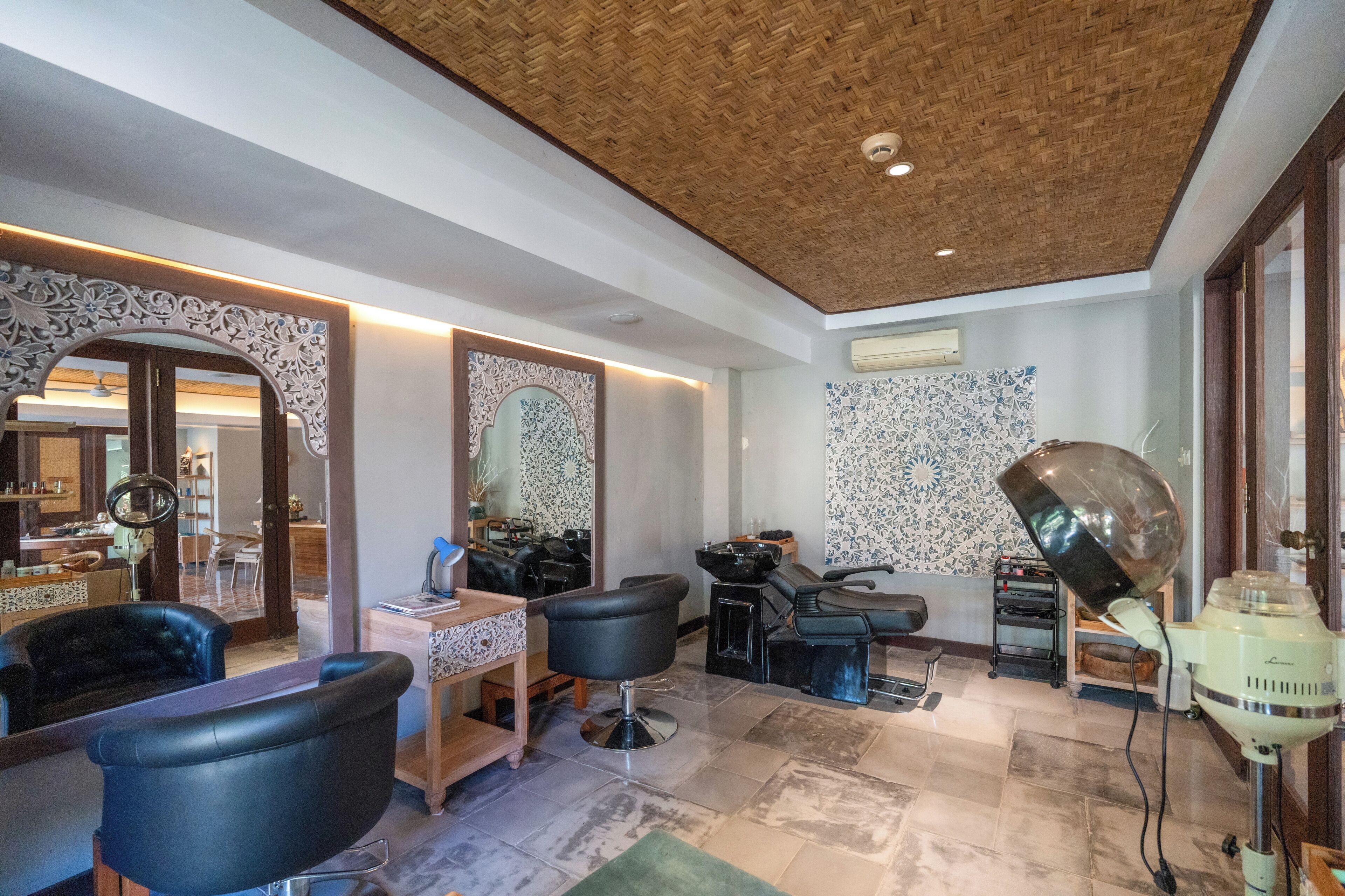 A salon with multiple black salon chairs, a wooden ceiling, and a patterned wall.