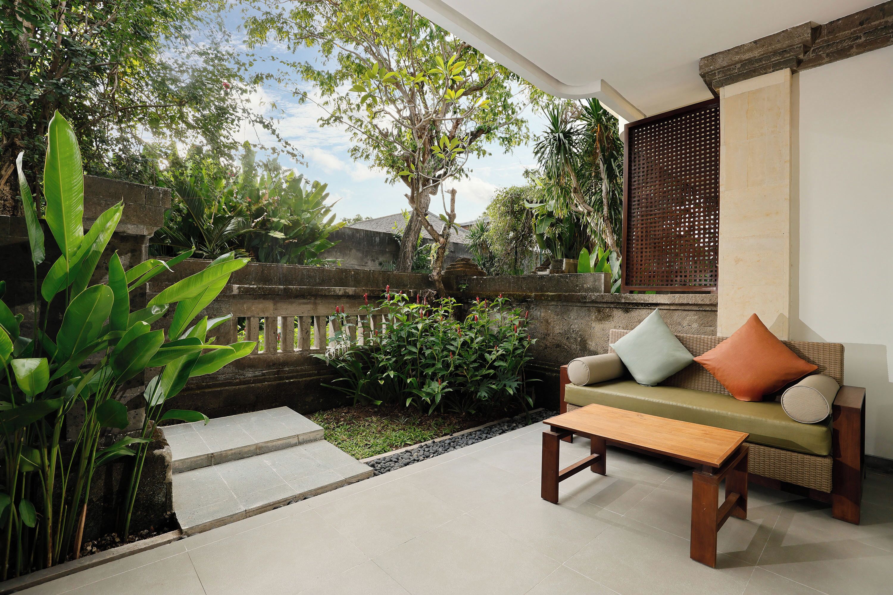 A patio with a sofa, a wooden table, and a small garden area with plants and a stone pathway.