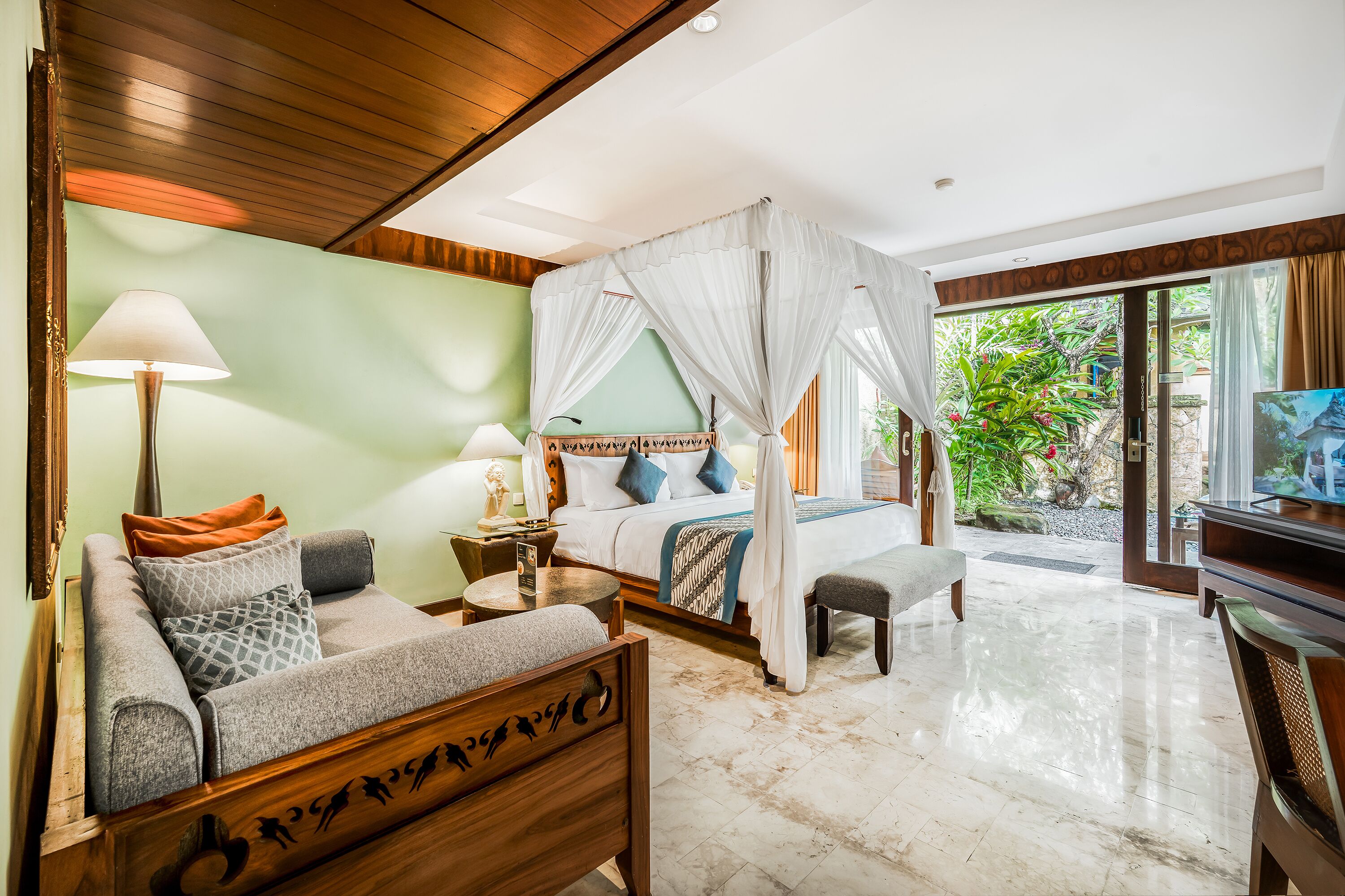 A bedroom with a bed, a sofa, a TV, and a view of greenery outside.