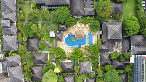 An aerial view of a resort with a central swimming pool, surrounded by lush greenery and thatched-roof buildings. - Rama Beach Resort and Villas (Kuta)