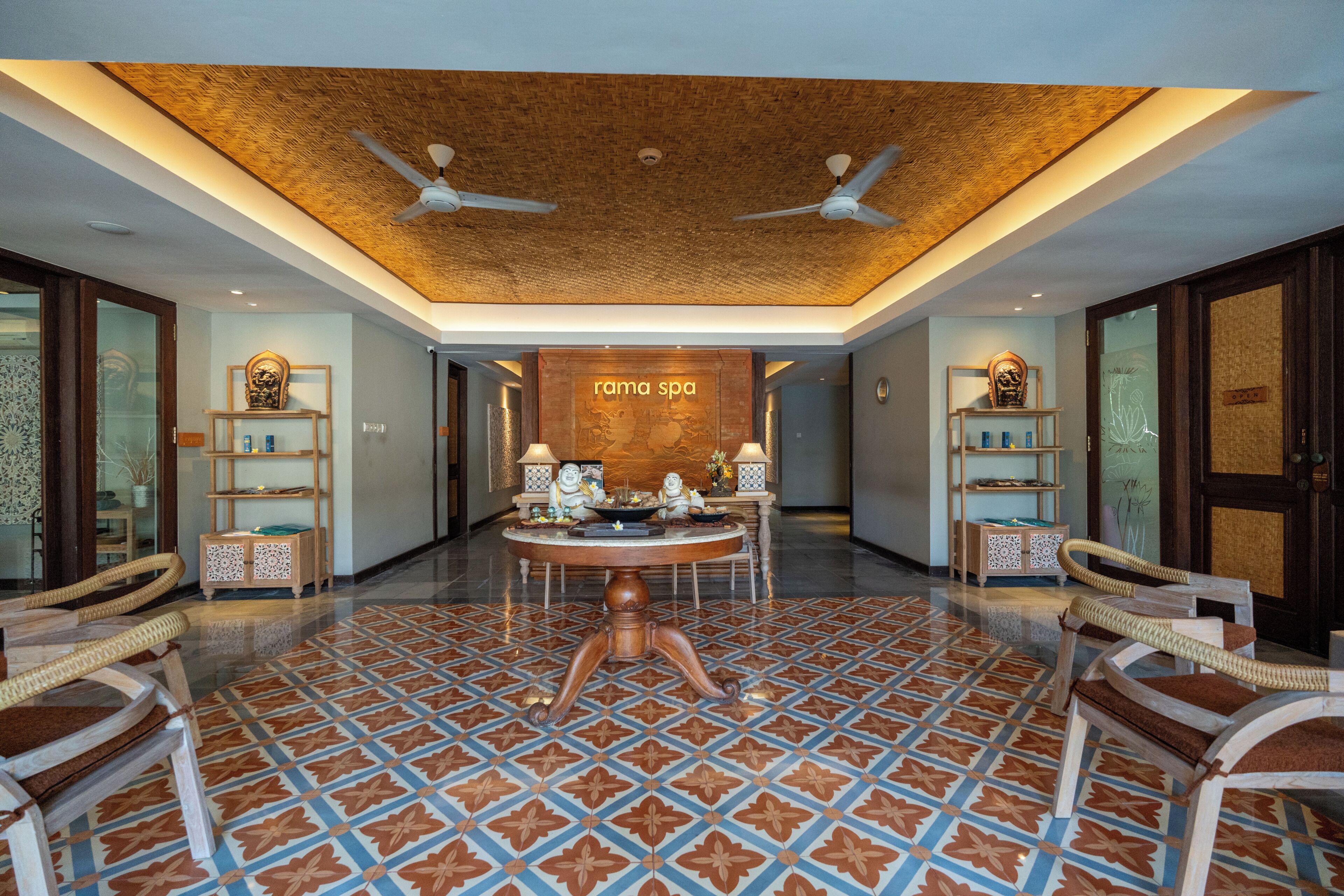 Eine geräumige Lobby mit einem gemusterten Boden, einem runden Tisch in der Mitte und Deckenventilatoren.