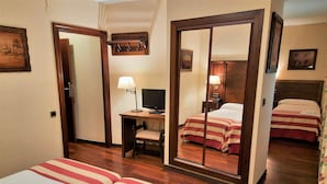 Habitación de hotel con dos camas, un escritorio con computadora, una silla, un espejo y un estante pequeño con ganchos.