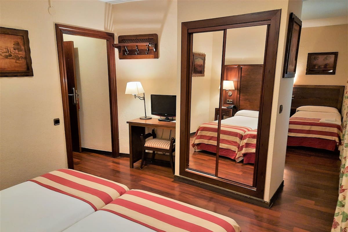 Hotelkamer met twee bedden, een bureau met een computer, een stoel, een spiegel en een klein plankje met haken.