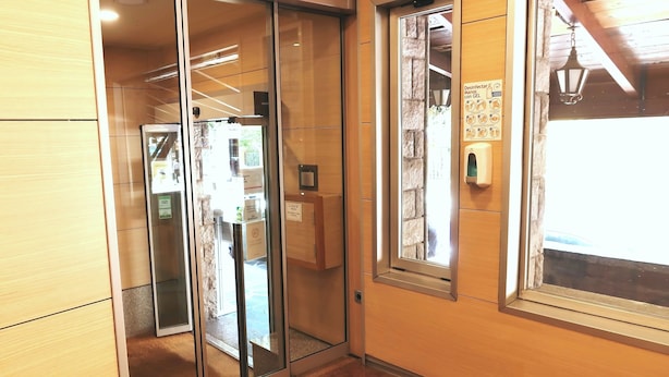 Un pasillo con una puerta de vidrio que da a una habitación, una ventana y una pared de piedra, además de un dispensador de gel antibacterial.