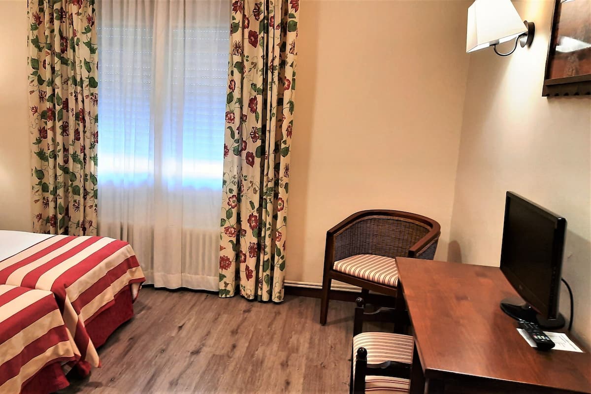 Een hotelkamer met een bed, een bureau met stoel, een televisie en gordijnen.