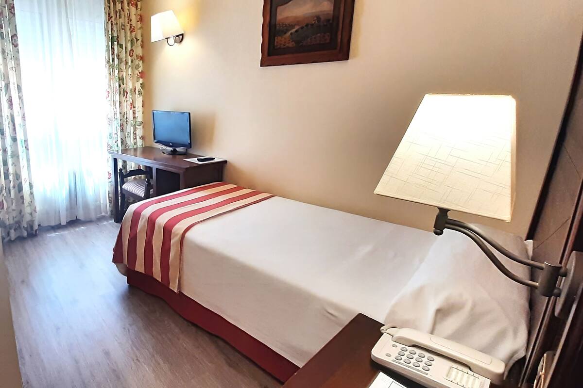 Een hotelkamer met een bed, een bureau met een computer, een telefoon en een schilderij aan de muur.