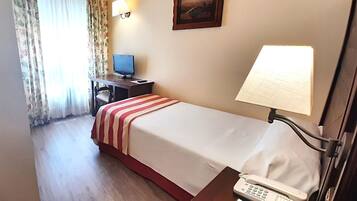 Habitación de hotel con una cama, un escritorio con computadora, un teléfono y un cuadro en la pared.