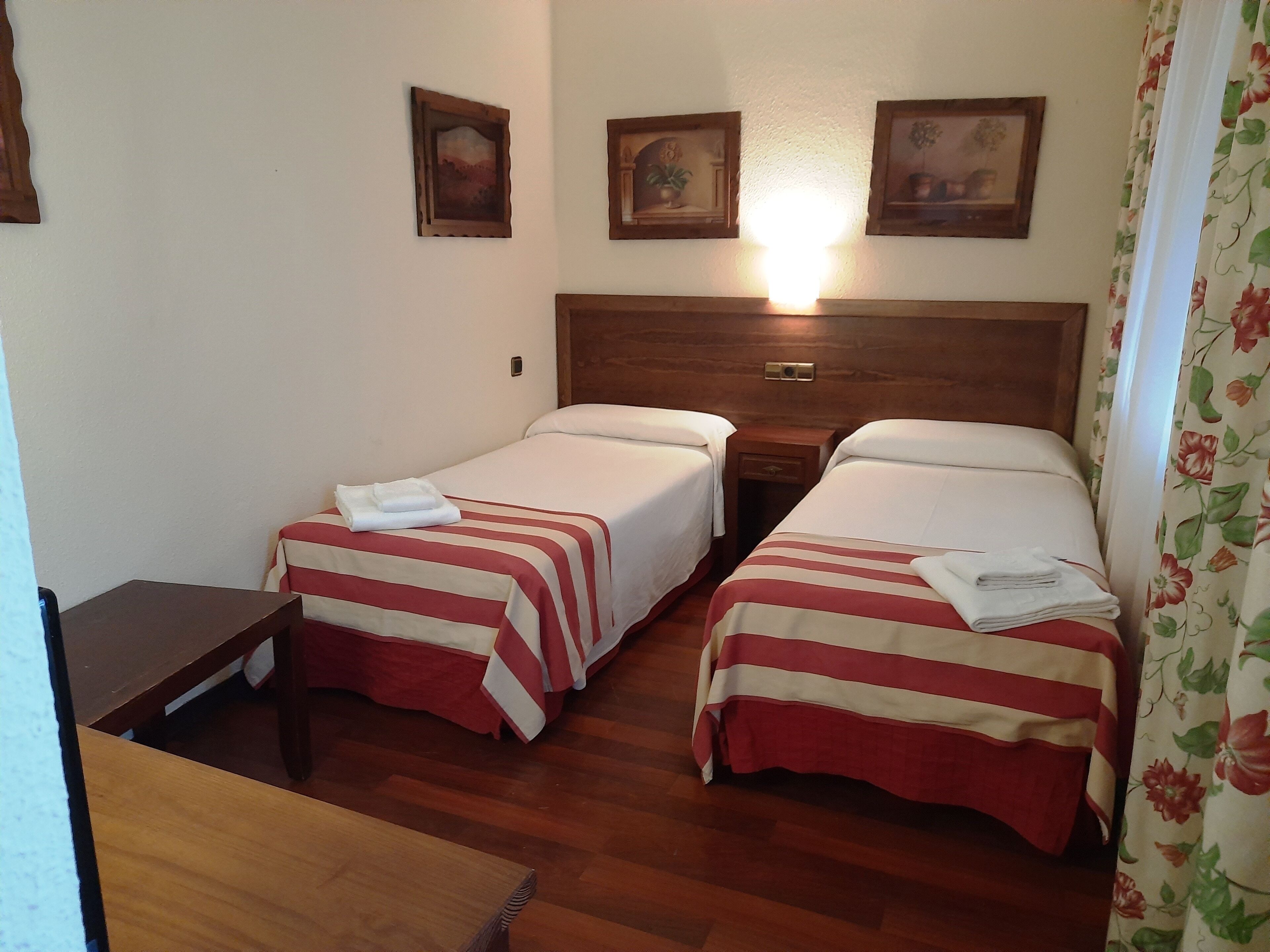 A hotel room with two beds, wooden headboards, and a small table.