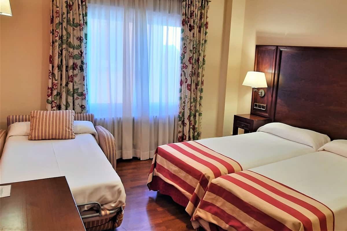 Een hotelkamer met twee bedden, bloemen gordijnen, een houten hoofdeinde en een nachtkastje met een lamp.