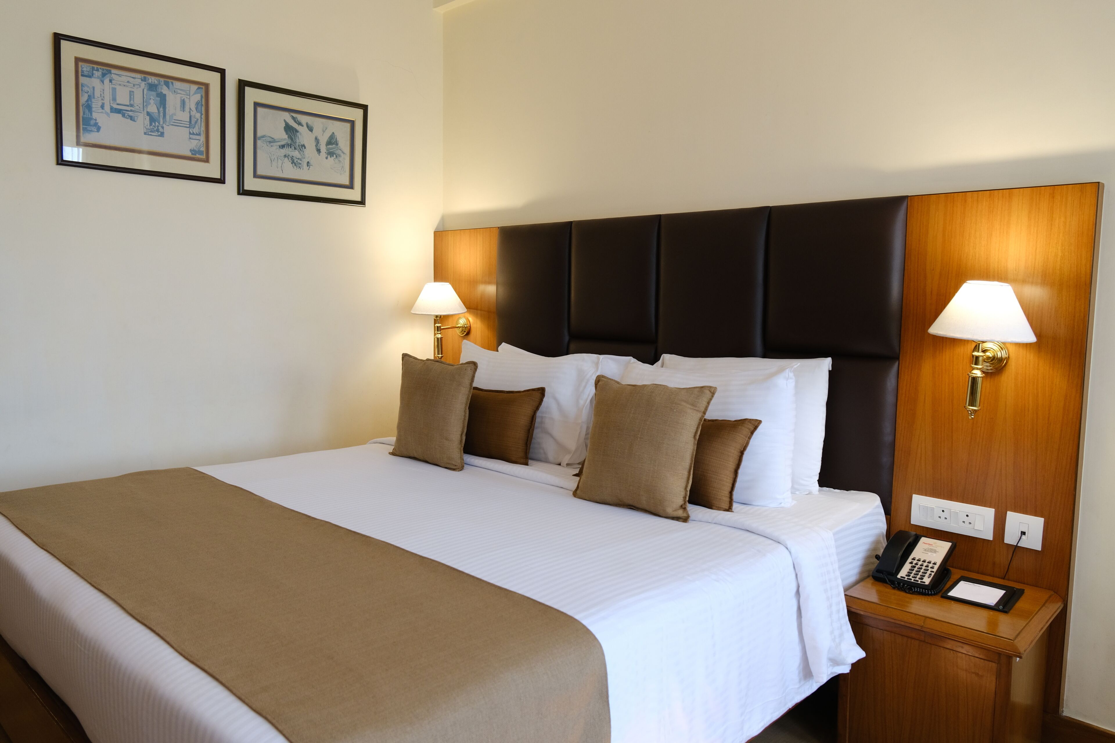 Habitación de hotel con una cama grande, dos lámparas de noche, un teléfono y dos cuadros en la pared.