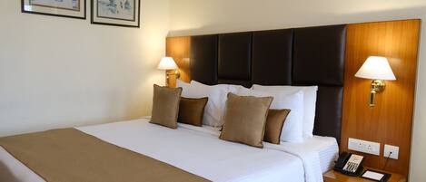 A hotel room with a large bed, two bedside lamps, a telephone, and two framed pictures on the wall.