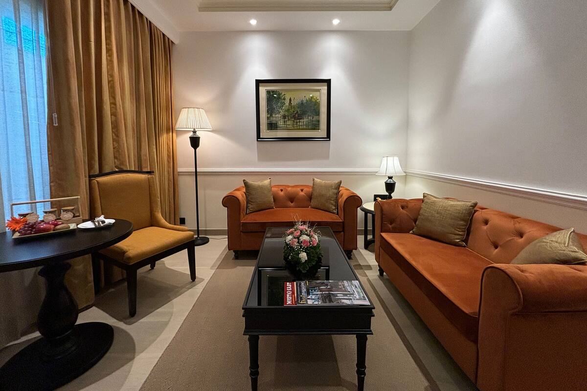 A living room with two orange sofas, a black coffee table with magazines, a floor lamp, and a painting on the wall.