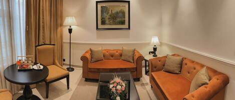 A living room with a sofa set, a coffee table with flowers, a side table with a lamp, and a framed picture on the wall.