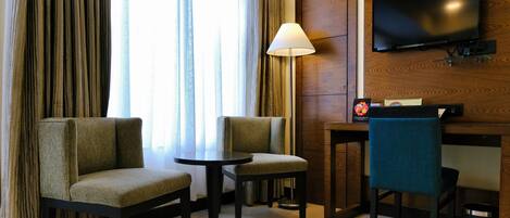 Habitación de hotel con dos sofás, una mesita, una lámpara, un televisor montado en la pared y un armario de madera.