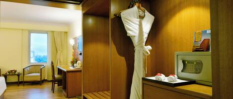 Habitación de hotel con techo de madera, una cama, un escritorio con una silla, una bata colgada en un perchero y un televisor sobre un pedestal.