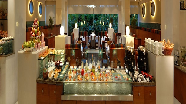 A buffet area with a variety of food options, a seating area with tables and chairs, and a decorative ceiling with skylights. - Peerless Hotel Kolkata (Kolkata)