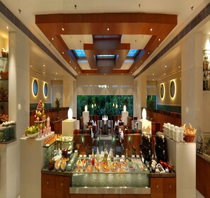 A buffet area with a variety of food options, a seating area with tables and chairs, and a decorative ceiling with skylights. - Peerless Hotel Kolkata (Kolkata)