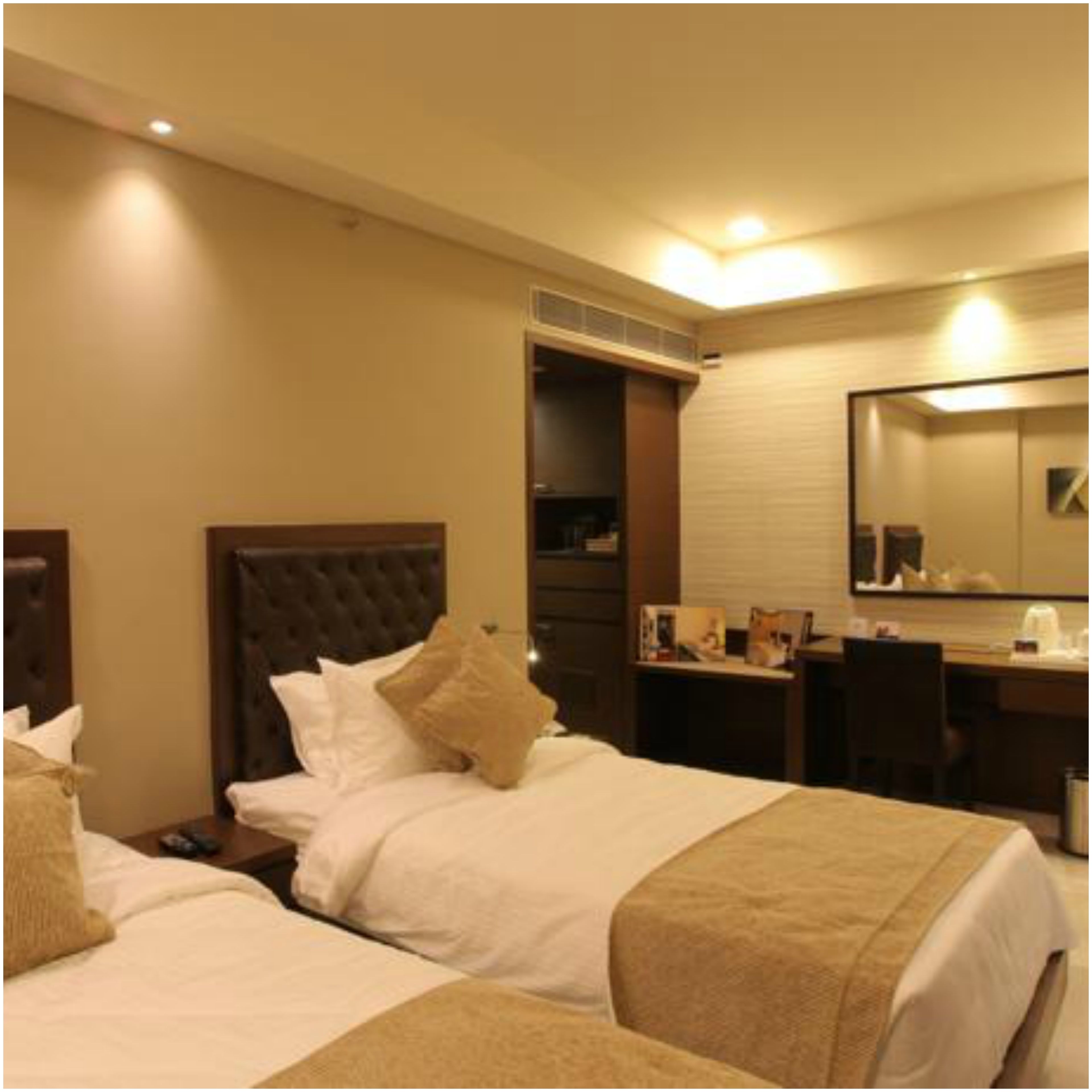 A hotel room with two beds, a desk, a chair, and a large mirror.