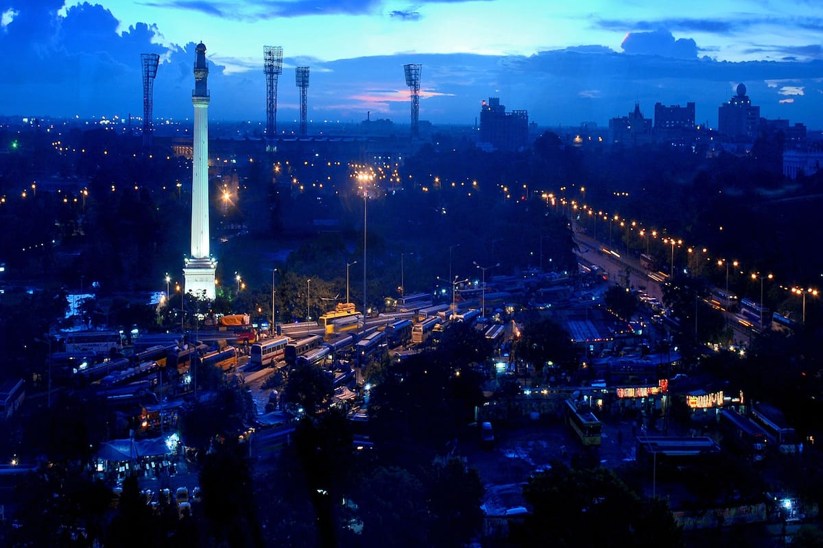 A nighttime cityscape with a prominent tower, busy streets, and distant buildings under a twilight sky.