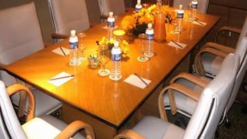 Un salón de conferencias con una larga mesa, seis sillas, botellas de agua, vasos y un jarrón con flores.