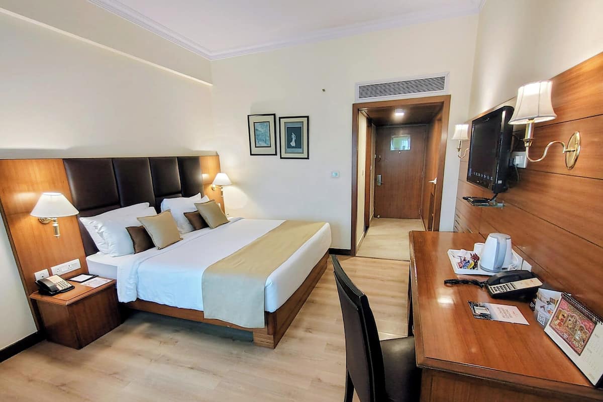 A hotel room with a bed, bedside tables, a desk with a chair, a television, and framed pictures on the wall.