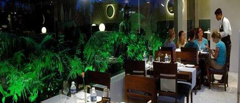 Un restaurante con mesas dispuestas para comer, un camarero atendiendo a los comensales y vistas del cielo nocturno a través de amplios ventanales.