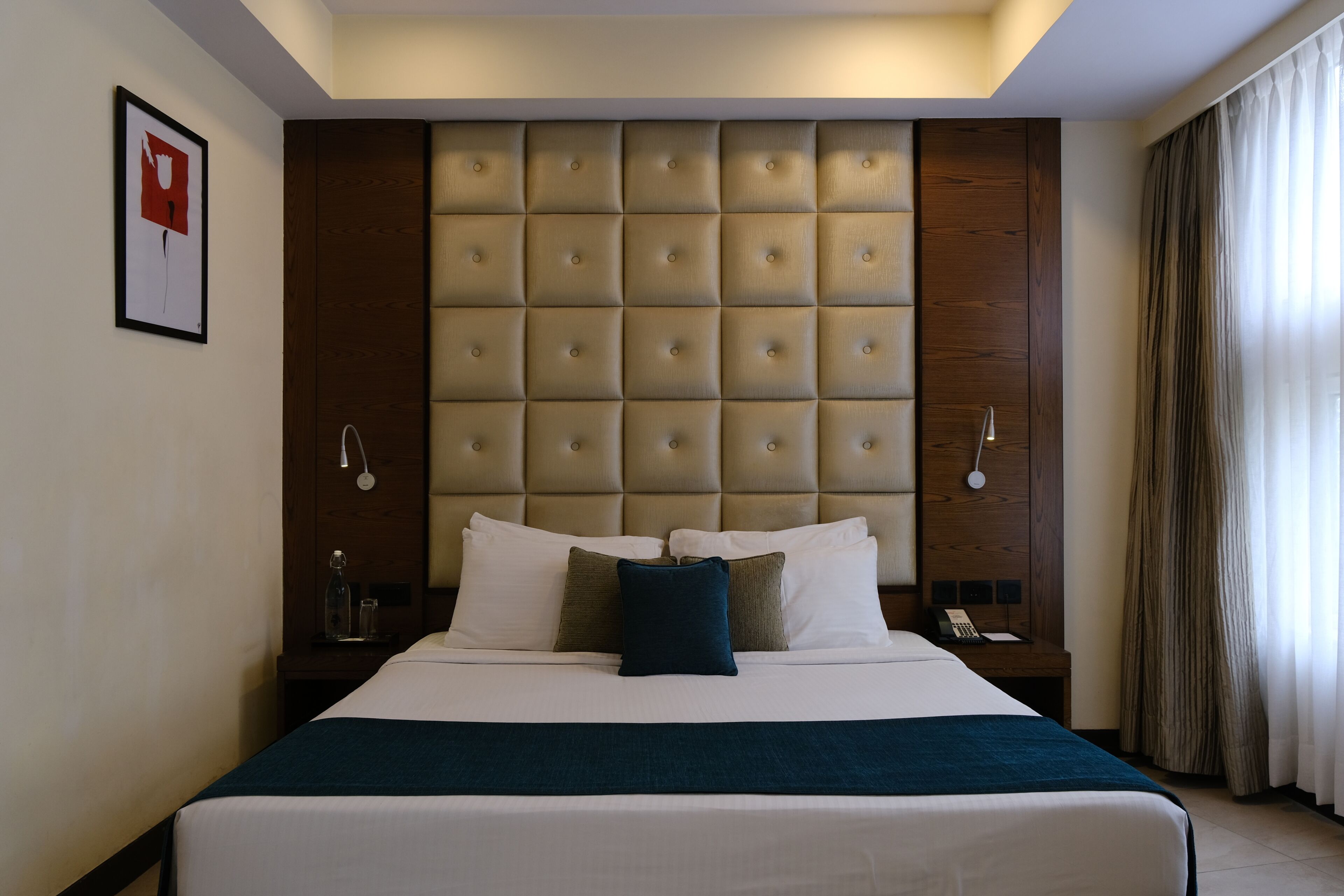 A hotel room with a large bed, a headboard with a tufted design, bedside tables with lamps, and a framed picture on the wall.