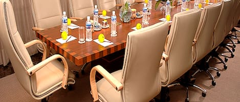 Une salle de conférence avec une longue table, de nombreuses chaises, des bouteilles d’eau et un vase rempli de fleurs.