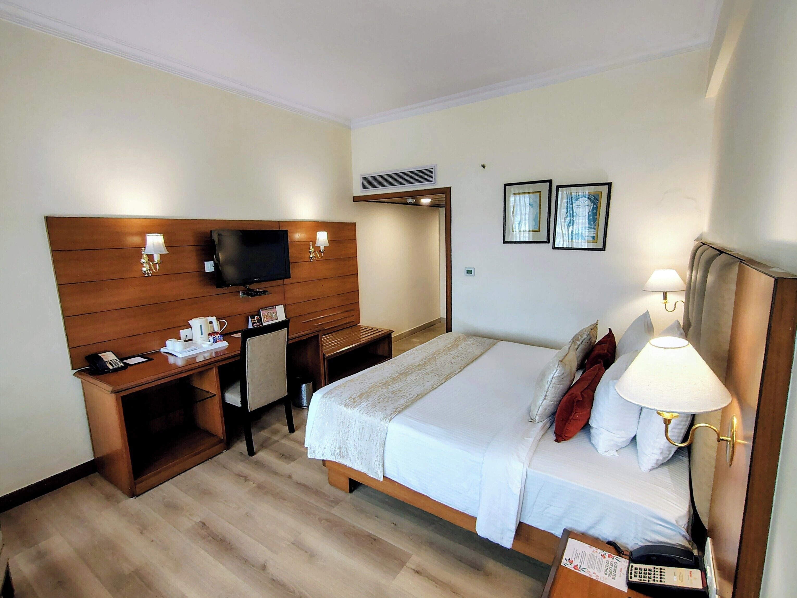 A hotel room with a bed, a desk with a TV, a telephone, and a lamp.